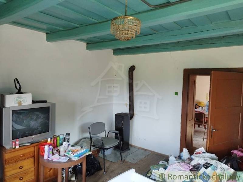 Veľký, vyše 4,5Ha slnečný pozemok s chalupou v strede, na lazoch, pri  - Interiér chaty s kachľami, starším televízorom, nábytkom a stropom modrej farby.