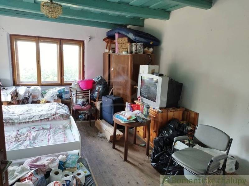 Veľký, vyše 4,5Ha slnečný pozemok s chalupou v strede, na lazoch, pri  - Interiér chaty s posteľou, televízorom, stoličkami a podlahou s dreveným dekorom.