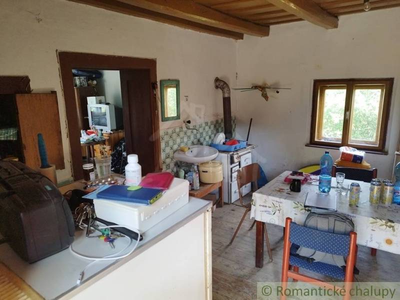 Veľký, vyše 4,5Ha slnečný pozemok s chalupou v strede, na lazoch, pri  - Chata s rustikálnym nábytkom, podlaha s dreveným dekorom, kuchynský kút, stôl s fľašami.