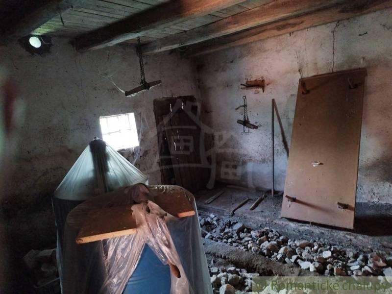 Veľký, vyše 4,5Ha slnečný pozemok s chalupou v strede, na lazoch, pri  - Interiér chaty so starými drevenými trámami, oknom a nábytkom pokrytým plachtou.