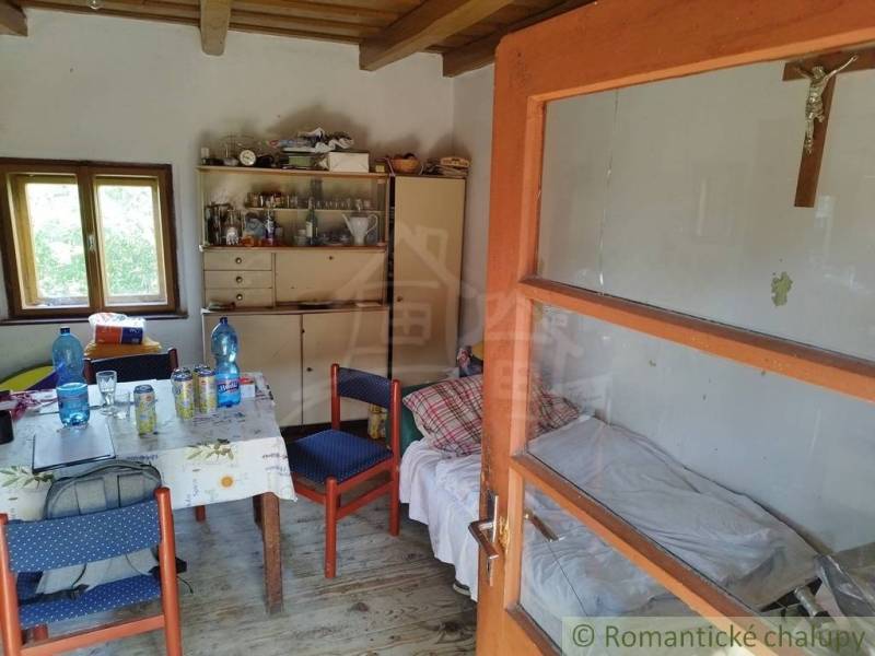 Veľký, vyše 4,5Ha slnečný pozemok s chalupou v strede, na lazoch, pri  - Interiér chaty s jedálenským stolom, kreslami, posteľou a skrinkou, podlaha s dreveným dekorom.
