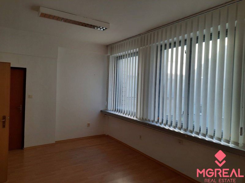 Prenájom kancelárií 21 m2 v centre Trnavy - Kancelária s podlahou s dreveným dekorom, vertikálnymi žalúziami a stropným osvetlením.