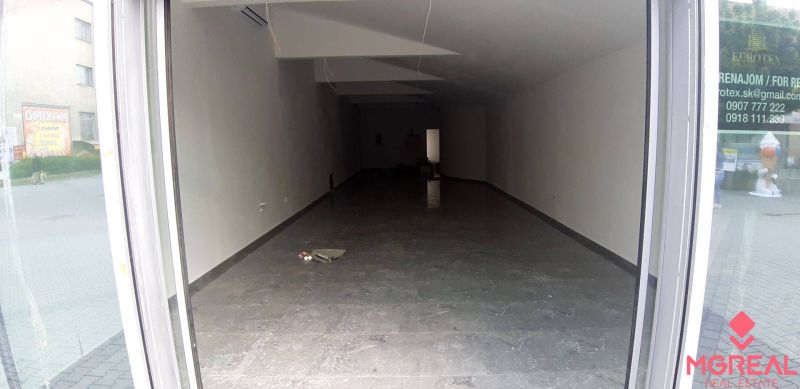Priestor do prenájmu v centre Topoľčian - Prázdne obchodné priestory s dlažbou a veľkými presklenými dverami.