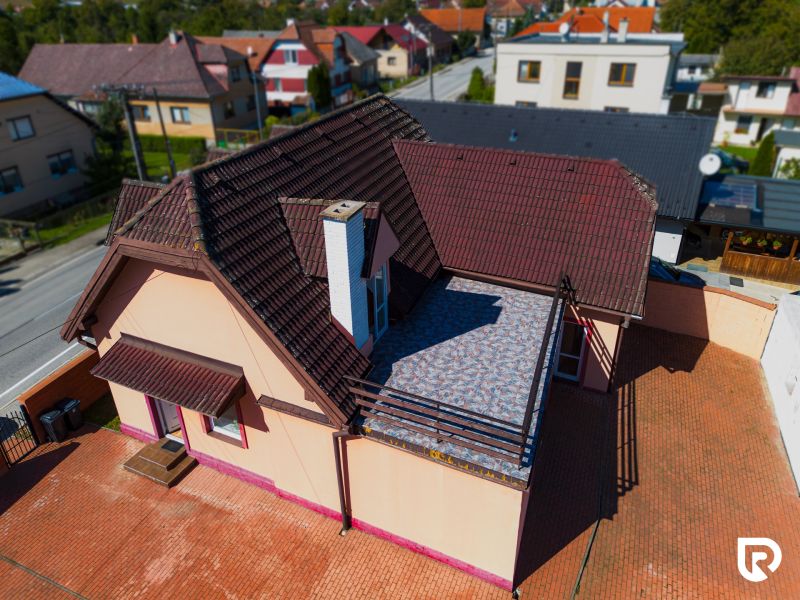 6-izbový rodinný dom s pozemkom 2218m2  | Horňany - Rodinný dom v Horňanoch s červenohnedou strechou a terasou, okolie z dlažby.