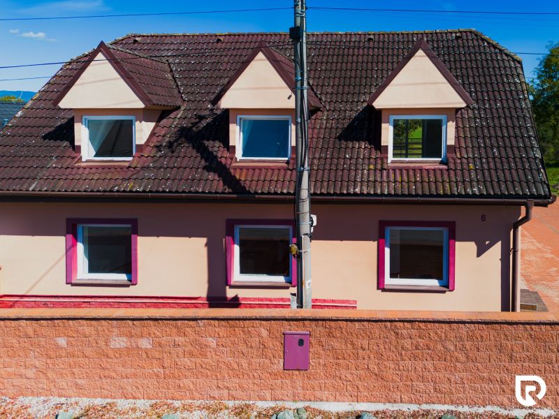 6-izbový rodinný dom s pozemkom 2218m2  | Horňany - Rodinný dom v Horňanoch s červenou strechou a omietkou v odtieni ružovej.