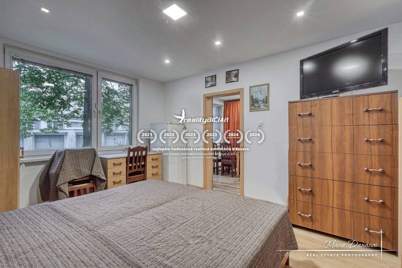 3-izbový byt v Šali na Vajanského ulici - Spálňa v 3-izbovom byte s posteľou, zásuvkami a televízorom na stene.