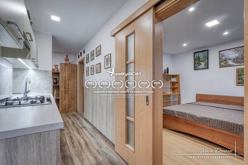 3-izbový byt v Šali na Vajanského ulici - Kuchynský kút s varnou doskou a posteľou, 3-izbový byt s podlahou s dreveným dekorom.