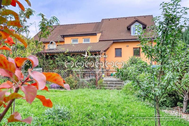 5-izbový rodinný dom s dvomi garážami v obci Špačince - Rodinný dom v Špačinciach na Špačinskej ulici s upravenou záhradou a oranžovou fasádou.