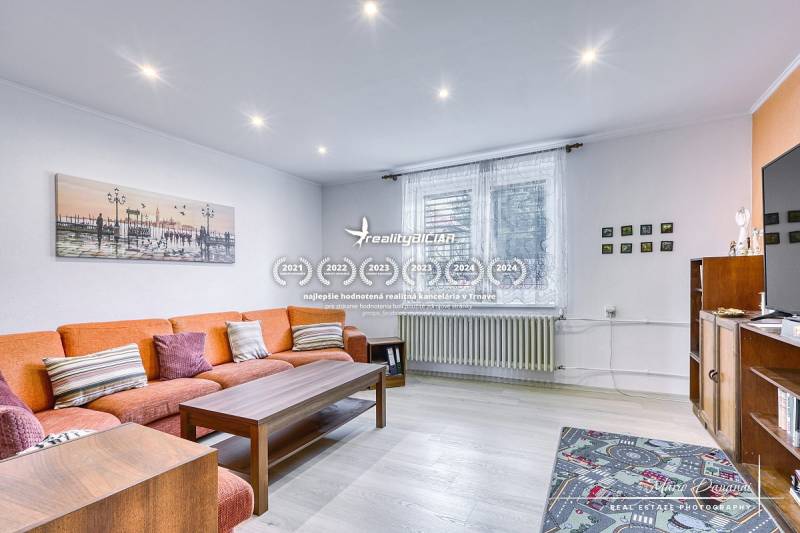 5-izbový rodinný dom s dvomi garážami v obci Špačince - Obývacia izba v rodinnom dome s oranžovou pohovkou a podlahou s dreveným dekorom.