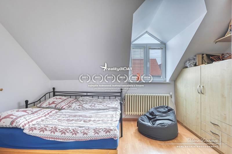 5-izbový rodinný dom s dvomi garážami v obci Špačince - Spálňa v rodinnom dome s posteľou, vreckovým kreslom a podlahou s dreveným dekorom.