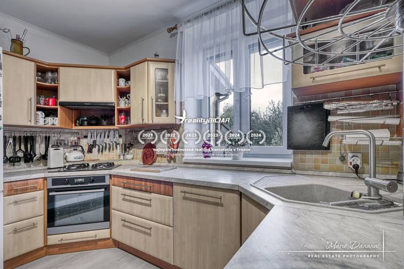 5-izbový rodinný dom s dvomi garážami v obci Špačince - Kuchyňa v rodinnom dome s kuchynskou linkou, sporákom a výhľadom cez okno.