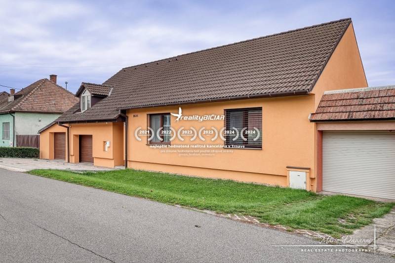 5-izbový rodinný dom s dvomi garážami v obci Špačince - Rodinný dom na ulici v Špačinciach so sedlovou strechou a oranžovou fasádou.