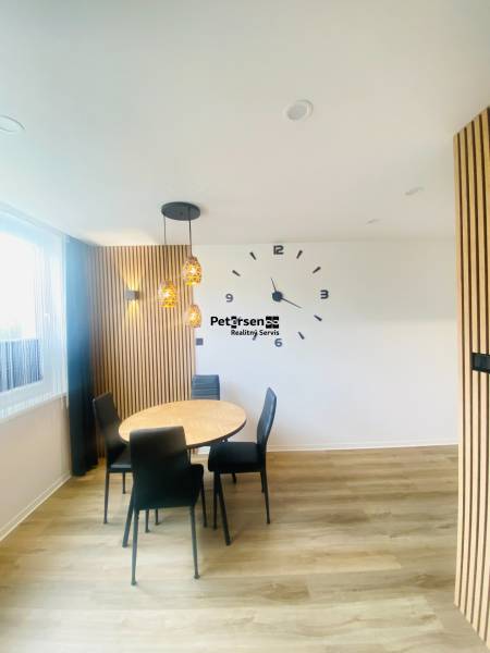 NA PRENÁJOM NOVOZREKONŠTRUOVANÝ 2-IZBOVÝ BYT, UL. ROŽŇAVSKÁ - Jedálenský kút s nástennými hodinami, drevené obklady a podlaha s dreveným dekorom.