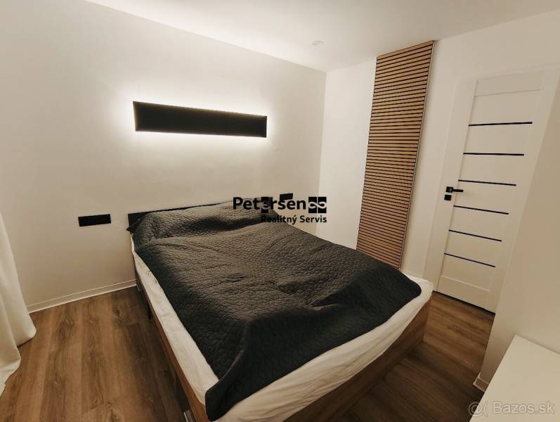 NA PRENÁJOM NOVOZREKONŠTRUOVANÝ 2-IZBOVÝ BYT, UL. ROŽŇAVSKÁ - Spálňa v 2-izbovom byte s posteľou, čiernymi detailmi a podlahou s dreveným dekorom.