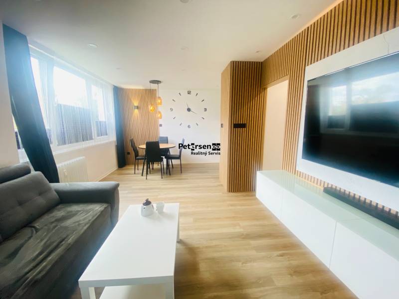 NA PRENÁJOM NOVOZREKONŠTRUOVANÝ 2-IZBOVÝ BYT, UL. ROŽŇAVSKÁ - Obývacia izba 2-izbového bytu s podlahou s dreveným dekorom, sedačkou a jedálenským kútom.