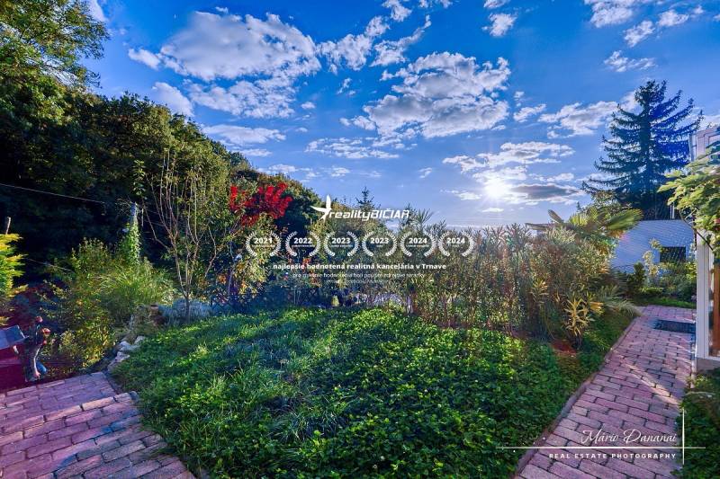 7-izbový rodinný dom s úžasným výhľadom v prestížnej lokalite Devín - Záhrada chaty v Bratislave - Devíne s chodníkom a bujnou výsadbou pod modrou oblohou.