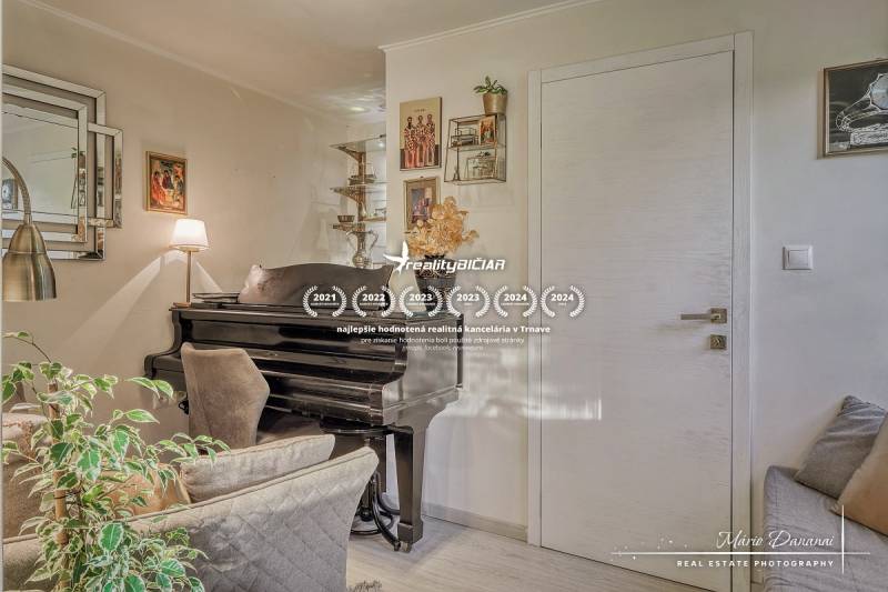 Rekreačná chata s úžasným výhľadom v prestížnej lokalite Devín - Interiér rodinného domu s pianom, kreslom a dekoračnými rastlinami, podlaha s dreveným dekorom.