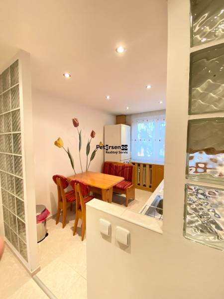 NA PRENÁJOM PRIESTRANNÝ 3-IZBOVÝ BYT V SKVELEJ LOKALITE, UL. SLOBODY - Jedálenský kút v 3-izbovom byte s dreveným stolom a červenými stoličkami.