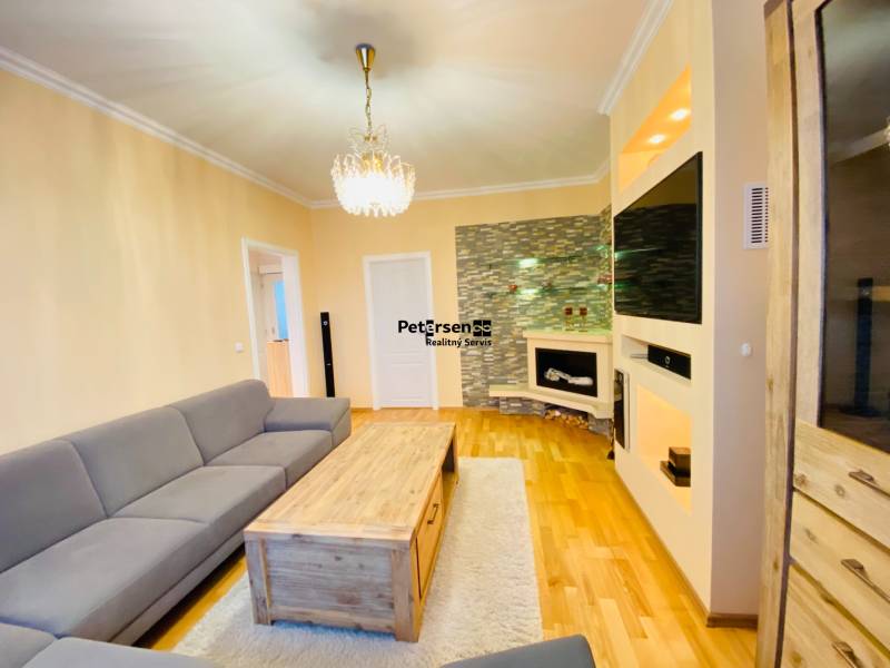 NA PRENÁJOM PRIESTRANNÝ 3-IZBOVÝ BYT V SKVELEJ LOKALITE, UL. SLOBODY - Obývacia izba v 3-izbovom byte s podlahou s dreveným dekorom, krbom a sedačkou.