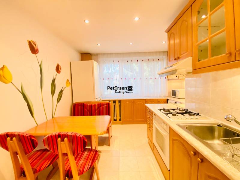 NA PRENÁJOM PRIESTRANNÝ 3-IZBOVÝ BYT V SKVELEJ LOKALITE, UL. SLOBODY - Kuchyňa v 3-izbovom byte s jedálenským stolom a nástennými dekoráciami tulipánov.