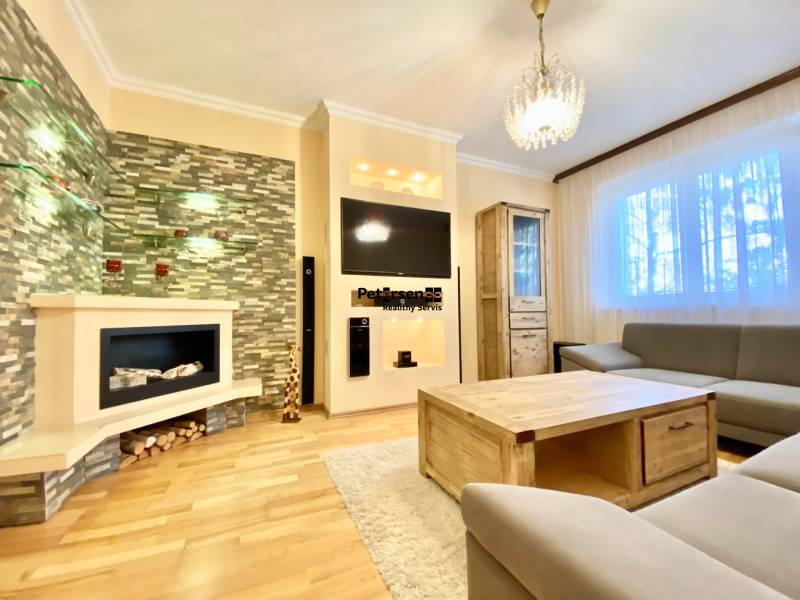 NA PRENÁJOM PRIESTRANNÝ 3-IZBOVÝ BYT V SKVELEJ LOKALITE, UL. SLOBODY - Obývačka v 3-izbovom byte s krbom, pohovkou a podlahou s dreveným dekorom.