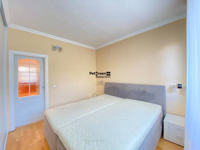 NA PRENÁJOM PRIESTRANNÝ 3-IZBOVÝ BYT V SKVELEJ LOKALITE, UL. SLOBODY - Spálňa s veľkou posteľou, nočnými stolíkmi a podlahou s dreveným dekorom v 3-izbovom byte.