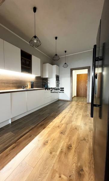 NA PRENÁJOM NADŠTANDARDNÝ 2-IZBOVÝ BYT V CENTRE MESTA - Kuchyňa v 2-izbovom byte s bielymi skrinkami a podlahou s dreveným dekorom.