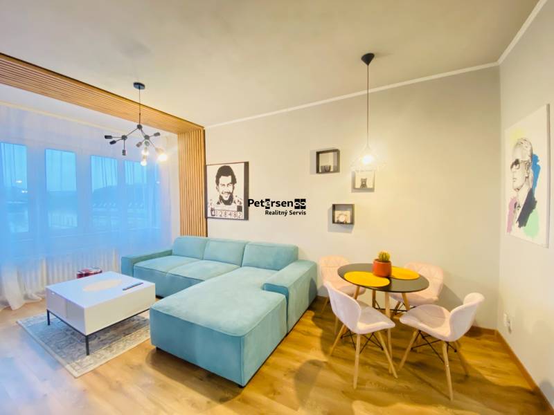 NA PRENÁJOM NADŠTANDARDNÝ 2-IZBOVÝ BYT V CENTRE MESTA - Obývacia izba v 2-izbovom byte s modrým gaučom a podlahou s dreveným dekorom.