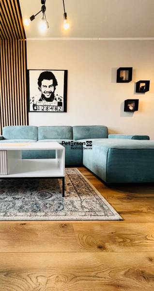 NA PRENÁJOM NADŠTANDARDNÝ 2-IZBOVÝ BYT V CENTRE MESTA - Obývačka v 2-izbovom byte s tyrkysovým gaučom, obrazom a podlahou s dreveným dekorom.