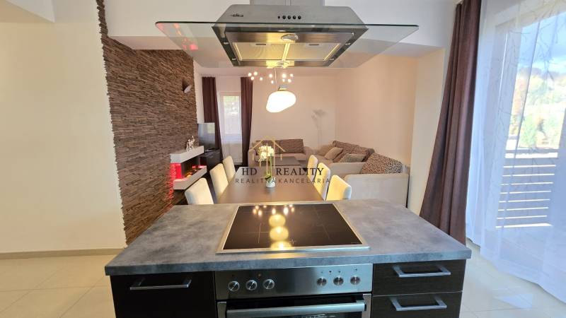 HD REALITY, Vám ponúka na Predaj 3-izbový Apartmán + Garážové státie - Kuchyňa v 3-izbovom byte s jedálenským stolom, tehlovým obkladom a podlahou s dreveným dekorom.