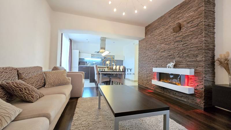 HD REALITY, Vám ponúka na Predaj 3-izbový Apartmán + Garážové státie - Interiér 3-izbového bytu s krbom, podlahou s dreveným dekorom a pohodlnou sedacou súpravou.