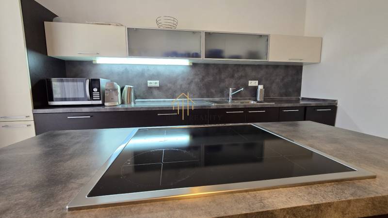 HD REALITY, Vám ponúka na Predaj 3-izbový Apartmán + Garážové státie - Kuchyňa v 3-izbovom byte s varnou doskou, mikrovlnkou a dreveným dekorom pracovnej dosky.