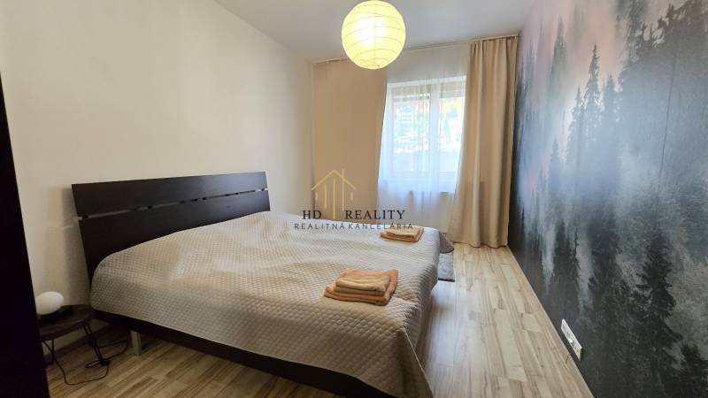 HD REALITY, Vám ponúka na Predaj 3-izbový Apartmán + Garážové státie - Spálňa s veľkou posteľou a stenou s lesnou tapetou, podlaha s dreveným dekorom.