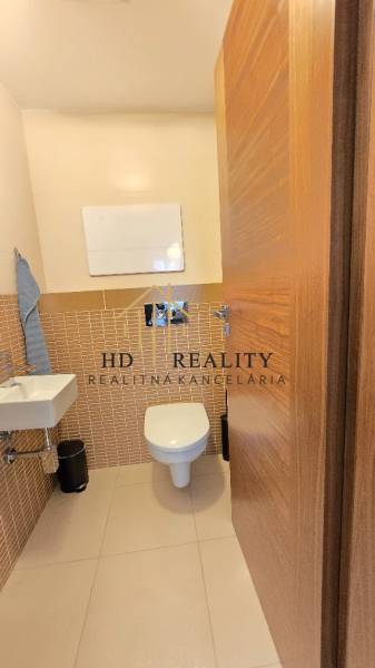 HD REALITY, Vám ponúka na Predaj 3-izbový Apartmán + Garážové státie - Kúpeľňa v 3-izbovom byte s podlahou s dreveným dekorom a nástenným umývadlom.
