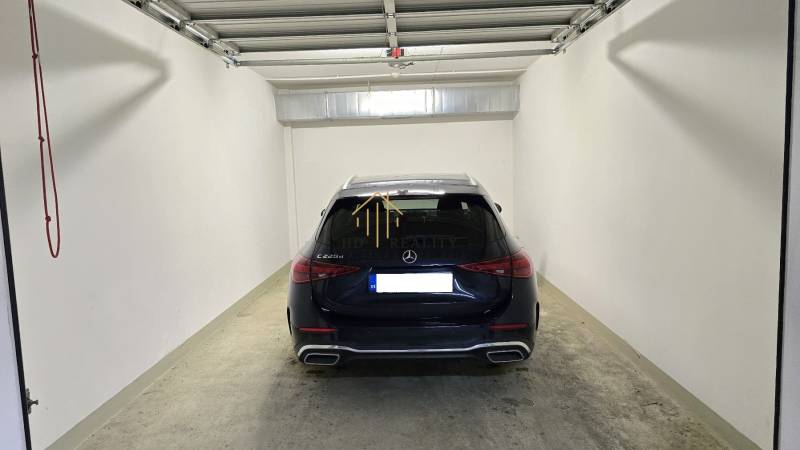 HD REALITY, Vám ponúka na Predaj 3-izbový Apartmán + Garážové státie - Garáž s autom Mercedes-Benz C223d s betónovou podlahou a bielymi stenami.