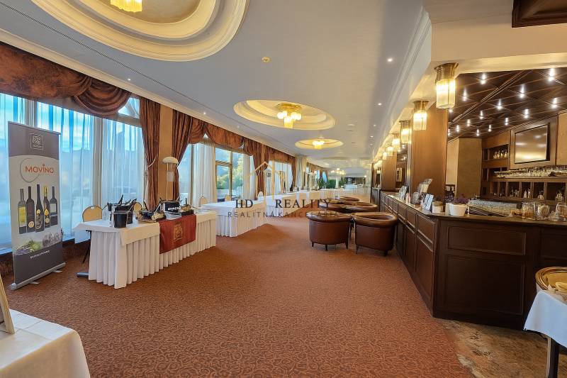 HD REALITY, Vám ponúka na Predaj 3-izbový Apartmán + Garážové státie - Luxusná miestnosť s barom, stolmi a koženými kreslami, podlaha s dreveným dekorom.