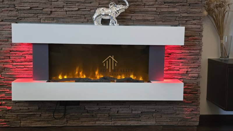 HD REALITY, Vám ponúka na Predaj 3-izbový Apartmán + Garážové státie - Elektrický krb s červeným podsvietením a dekoratívnym slonom na podlahe s dreveným dekorom.