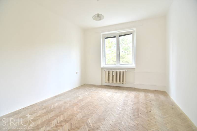 SEČOVSKÁ, 2-i tehlový byt, 56 m2, orientácia V a Z - OBKLOPENÝ ZELEŇOU - Prázdna izba s podlahou s dreveným dekorom, oknom a radiátorom v 2-izbovom byte.