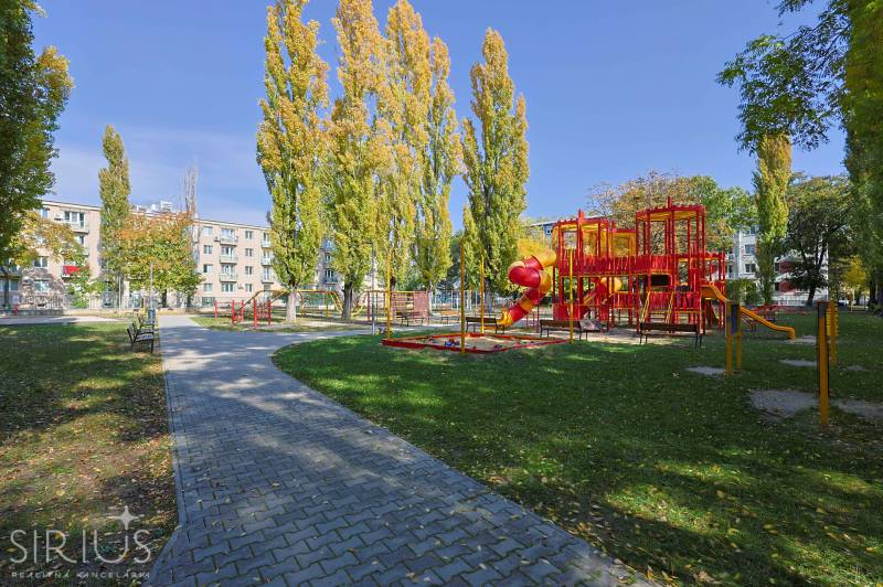 SEČOVSKÁ, 2-i tehlový byt, 56 m2, orientácia V a Z - OBKLOPENÝ ZELEŇOU - Detské ihrisko s červenými preliezačkami obklopené stromami na Sečovskej ulici v Ružinove, Bratislava.