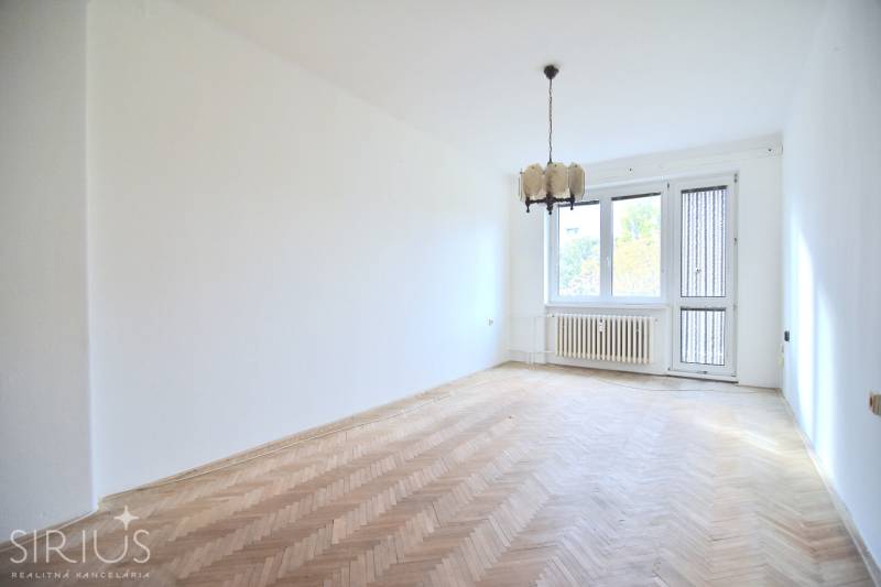 SEČOVSKÁ, 2-i tehlový byt, 56 m2, orientácia V a Z - OBKLOPENÝ ZELEŇOU - Obývacia izba s podlahou s dreveným dekorom v 2-izbovom byte ukazuje neutrálne biele steny.