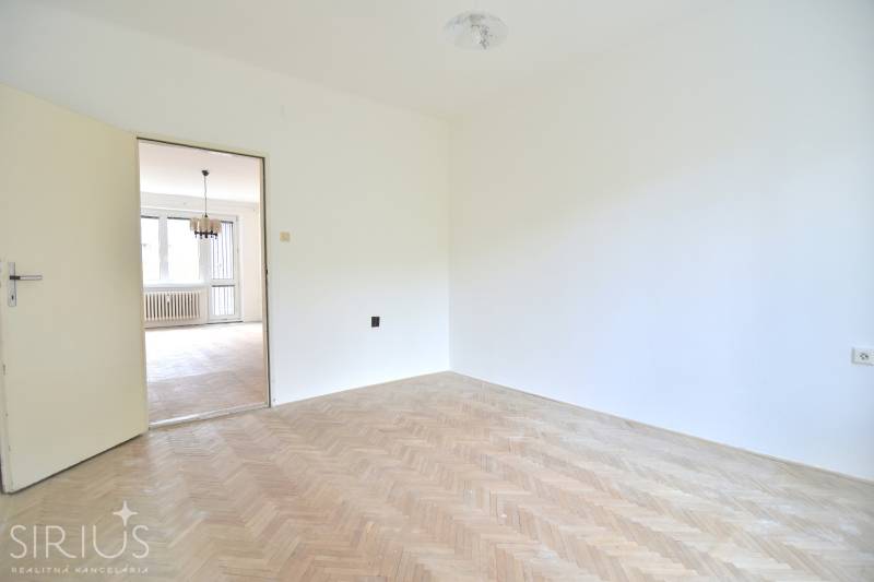 SEČOVSKÁ, 2-i tehlový byt, 56 m2, orientácia V a Z - OBKLOPENÝ ZELEŇOU - Biela miestnosť v 2-izbovom byte s podlahou s dreveným dekorom a výhľadom do obývacej izby.