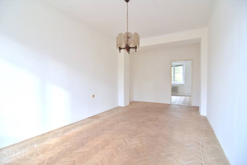 SEČOVSKÁ, 2-i tehlový byt, 56 m2, orientácia V a Z - OBKLOPENÝ ZELEŇOU - Priestranná izba v 2-izbovom byte s podlahou s dreveným dekorom a závesným svietidlom.