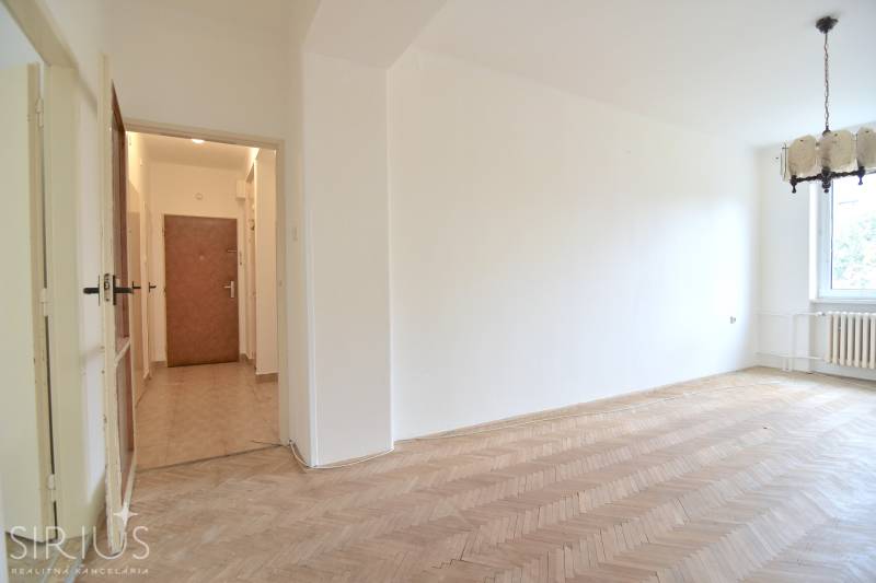 SEČOVSKÁ, 2-i tehlový byt, 56 m2, orientácia V a Z - OBKLOPENÝ ZELEŇOU - Obývačka v 2-izbovom byte s podlahou s dreveným dekorom a visiacim lustrom.