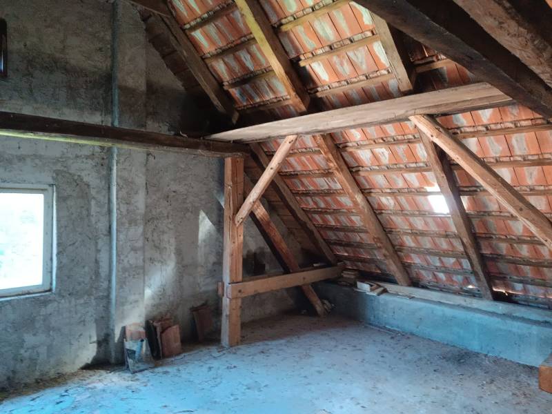 Hospodárska usadlosť  - Podkrovie rodinného domu so strešnými trámami a oknom.