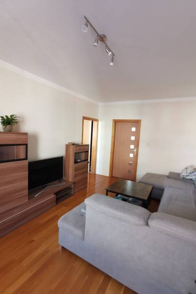 3 izbový byt Zlaté Moravce - Obývačka s podlahou s dreveným dekorom, sivou sedačkou a drevenou stenovou jednotkou, 3-izbový byt.