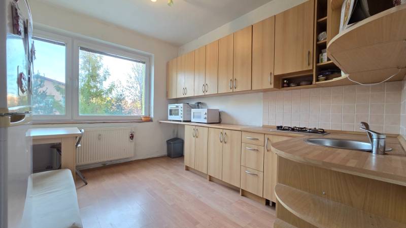 REZERVOVANÉ: NA PREDAJ -  1-izbový byt vo Veľkom Šariši - PREŠOV - Kuchyňa v 1-izbovom byte s podlahou s dreveným dekorom, drevenými skrinkami a veľkým oknom.