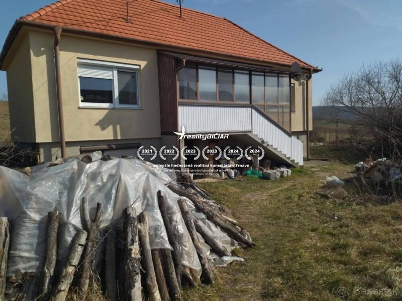 Rodinný dom v obci Dobrá Voda  - Rodinný dom v Dobrej Vode s drevenými polenami na oplocenom pozemku.