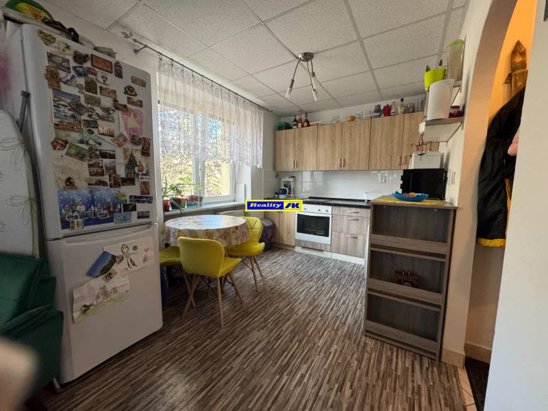 REZERVOVANÉ jednoizbový zrekonštruovaný byt v širšom centre mesta - Kuchyňa s podlahou s dreveným dekorom, jedálenským stolom a chladničkou v 1-izbovom byte.