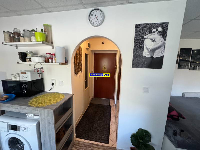 REZERVOVANÉ jednoizbový zrekonštruovaný byt v širšom centre mesta - Interiér 1-izbového bytu s podlahou s dreveným dekorom, poličkami a práčkou.