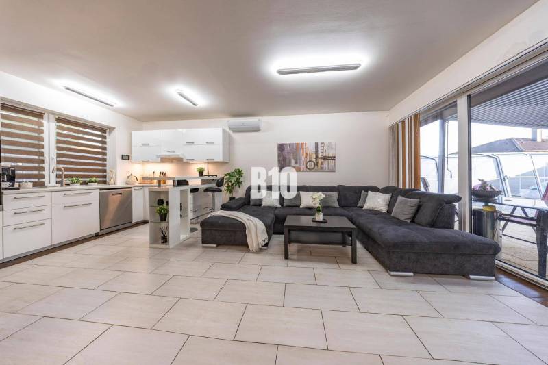 Tri Vody - 4-izbový rodinný dom s bazénom | Most pri Bratislave – Baza - Svetlá obývacia izba v rodinnom dome s kuchyňou a veľkou pohovkou.